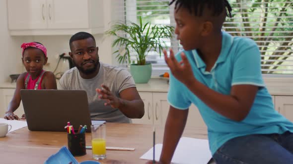 African american father using laptop and helping his son with homework at home