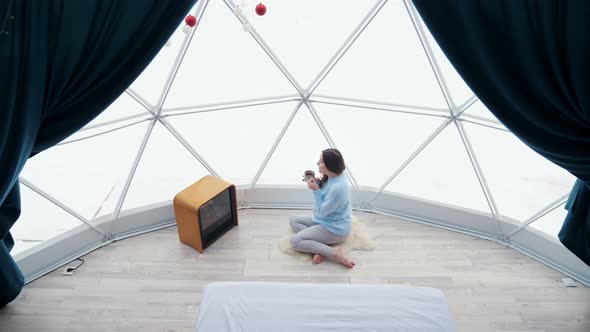 Pregnant Woman Sits on Rug Near Fireplace Enjoying Hot Drink