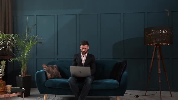 Portrait of an Elegant Businessman Sitting with Laptop on the Couch at the Luxury Blue Office