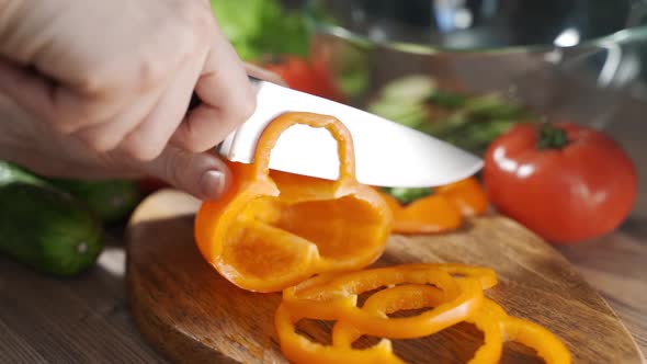 Closeup Female Cook Hands Chopping Pepper for Salad on a Wooden Board in the Kitchen