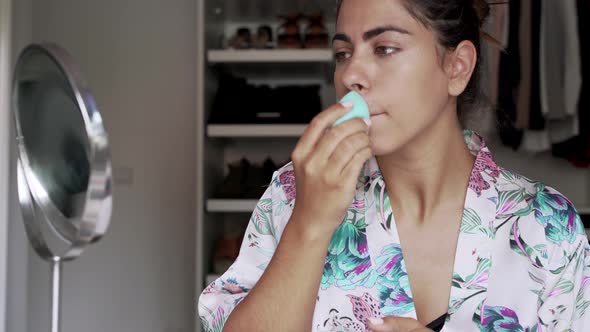 Young woman applying makeup with sponge