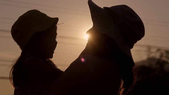 Silhouette of cute daughter hugging and kissing her loving mother at sunset at summer garden.