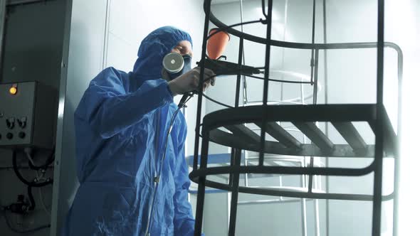 Worker painter in a respirator applies paint to metal frames in a production workshop