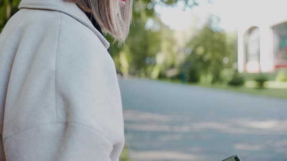 Girl Sits on a Park Bench Looking at the Phone Waving to a Friend and Smiling