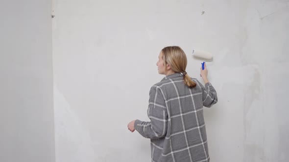 a Young Woman in a Gray Shirt Paints a Wall at Home with a Paint Roller