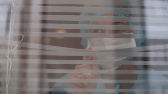 Nurse looking through window of hospital with disturbed look, coronavirus