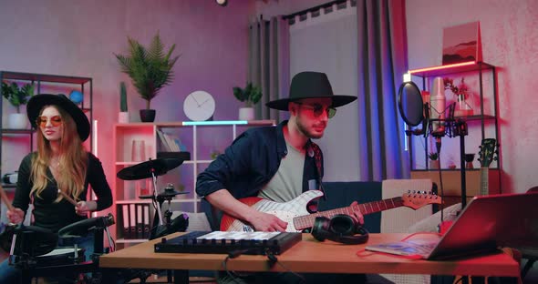 Guy and Girl Playing on Drums and Guitar During Preparation to the Concert in the Evening in Home