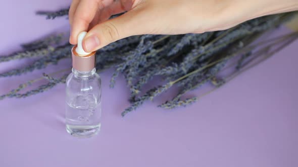 Lavender Essential Oil, Drop Falls From Cosmetic Pipette and Lavender Bouquet on Violet Background