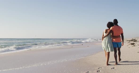 African american couple embracing together and walking on sunny beach