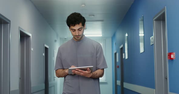 A Doctor Uses a Tablet While Walking Along the Corridor of the Medical Center