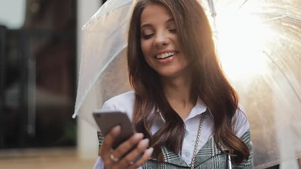 Beautiful Young Business Woman Using Smartphone on the Street in Rainy Weather, Smiling