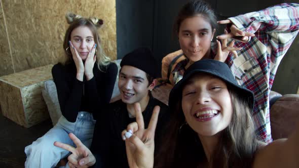 Four Teens Sitting on a Sofa and Waving to the Camera to Make Selfie