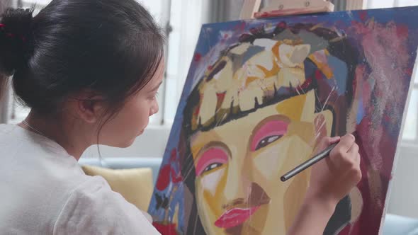 Close Up Side View Of An Asian Artist Girl Holding Paintbrush Painting A Girl's Face On The Canvas