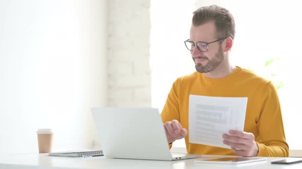 Man with Laptop Celebrating Success While Reading Documents