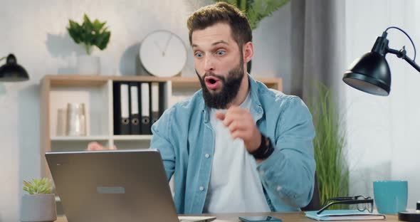 Bearded Guy Recieving Good News on Computer and Enjoying from Results with Raised Hands
