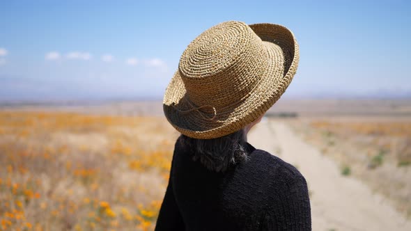 An old woman on a dirt road talking and gesturing with her hands in a field of orange flowers SLOW M