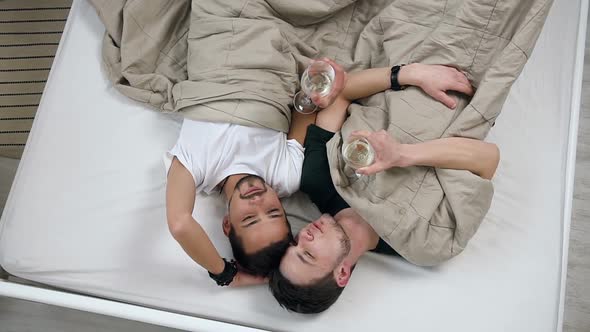 Happy Young Gay Men Couple Lying on Bed in Light Bedroom