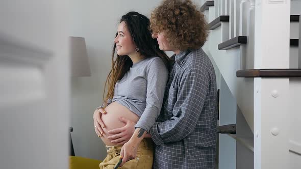 Pregnant Couple Enjoying Future Parenthood while Standing Together in front of the Window