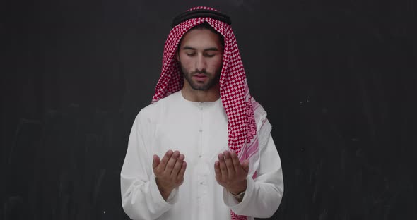 Man in Traditional Clothes in Front of Black Chalkboard Praying with Hands Wide Open