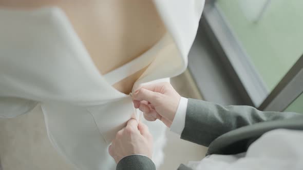 Husband buttoning dress on bride