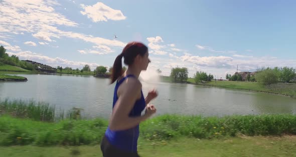 Camera runs along side, and then falls behind a fit woman going for a jog.