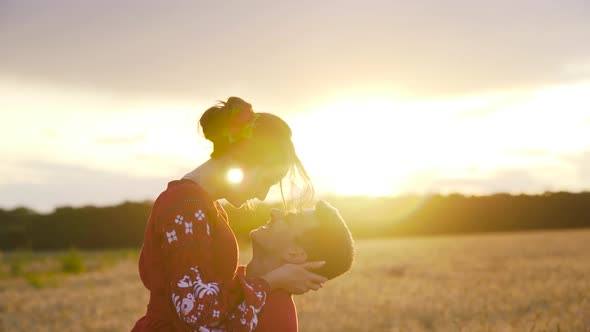 Young man kissing and spinning his girlfriend around on sunset in wheat field.
