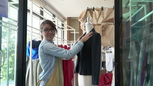 Happy young Asian woman dressmaker fashion designer is checking for completion for a suit and Dress