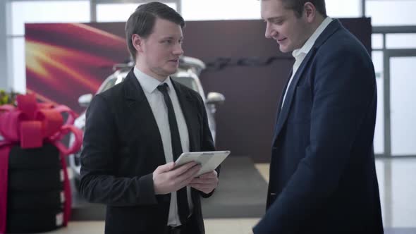 Portrait of Smiling Caucasian Car Dealer Welcoming Client in Showroom