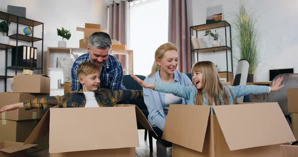 Parents Playing with their Son and Daughter which Sitting in Carton Boxes while Mom and Dad