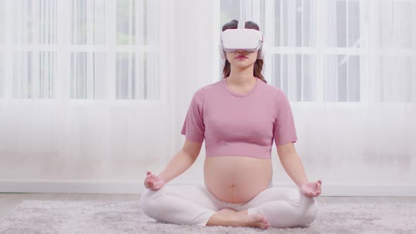 Happy Asian Pregnant woman using virtual reality glasses for practice yoga online class