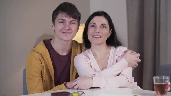 Middle Shot of Happy Caucasian Son and Mother Looking at Camera and Smiling As Sitting at the Table