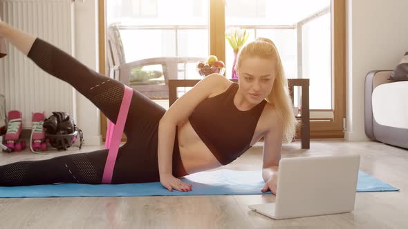 Young Sporty Beautiful Woman Exercising at Home in a Living Room. Using Laptop To Watch Online