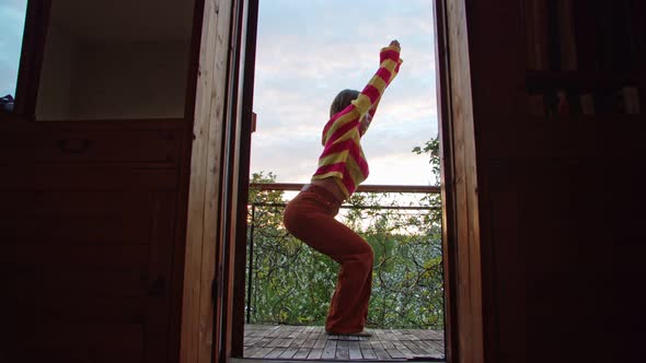 a Woman in a Sweater Does an Asana on Her Balcony Surrounded By Nature