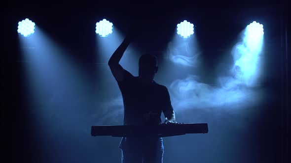 Musician Silhouette Playing on Synthesizer Piano Keyboard in Dark Studio with Neon Lighting. Neon