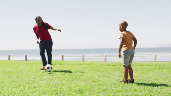 Video of happy african american father and son playing soccer outdoors and having fun