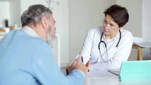 Serious Concentrated Caucasian Female Doctor Listening to Male Patient Complaints Writing Symptoms