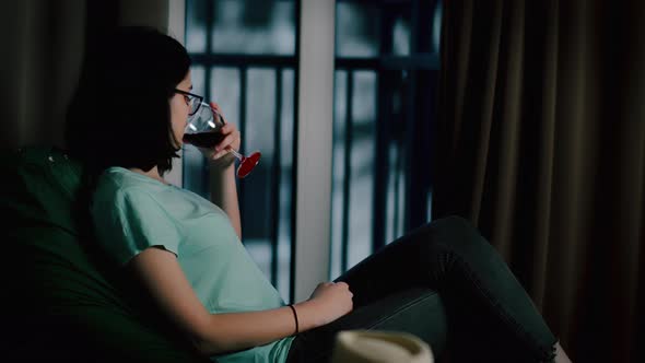 Pretty Girl with a Glass of Wine at Home in Front of the Window Cold Weather Outside the Window