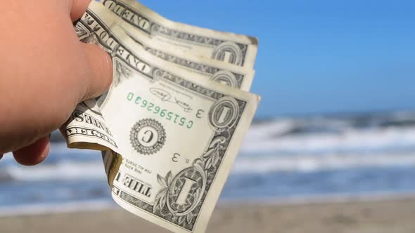 Person Holding Three Paper Dollar Bills on Background of Sea and Sea Waves