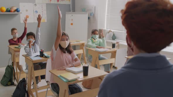 Children in Face Masks Raising Hands in Class