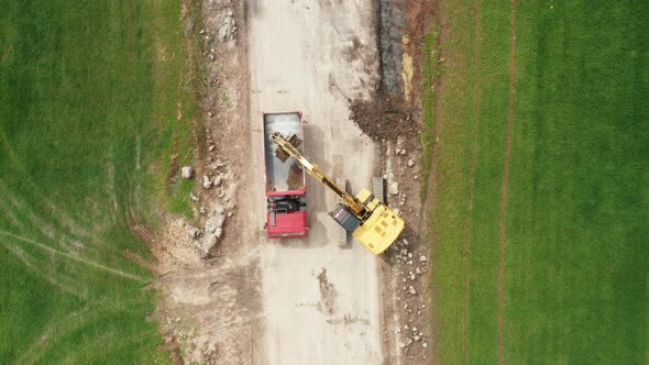 A Red Truck Pulls Up and a Yellow Excavator Loads the Soil From the Field Into the Body of a Dump