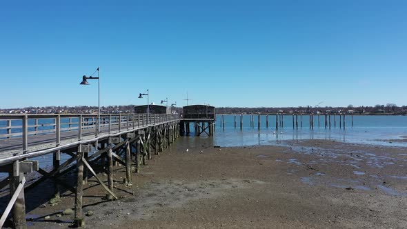 a low angle drone view during low tide. The drone camera dolly in next to an empty wooden pier on th