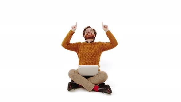 Handome Caucasian Bearded Brunet Man in a Soft Orange Knitted Sweater with a Laptop on His Knees
