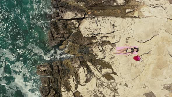 Aerial View Girl Sunbathing on a Rock By the Ocean