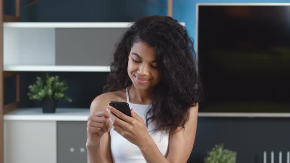 Young African Positive Woman Using Smartphone Surfing Social Media, Checking News, Texting Messages