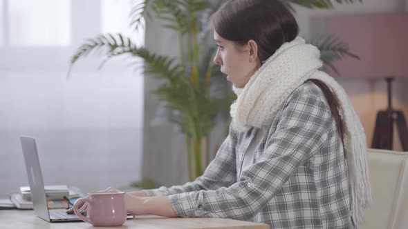 Portrait of Ill Caucasian Businesswoman in White Scarf Typing on Laptop Keyboard and Coughing