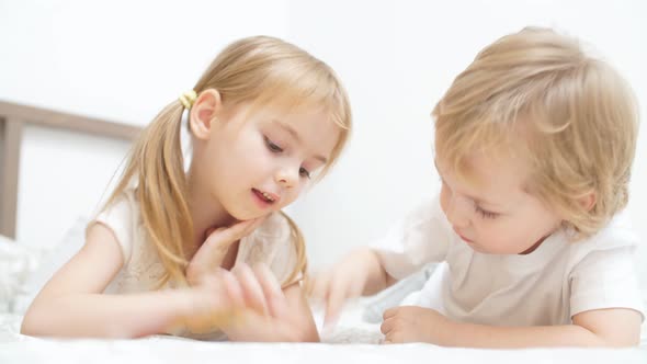 Cute Blond Kids Play Games on Tablet in a Light Room