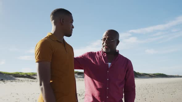 African american father standing on beach putting hand on shoulder of his teenage son and talking