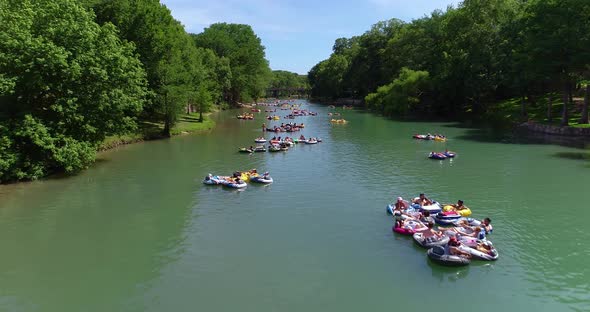 People tubing in groups down the Guadalupe river waving to the camera. This shot was taken in Canyon