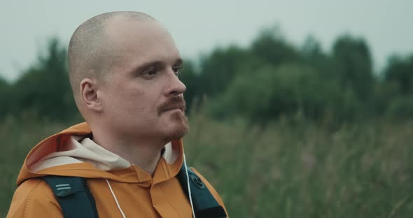 Man with Beard Dressed in an Orange Raincoat Admires View of Nature at Sunset