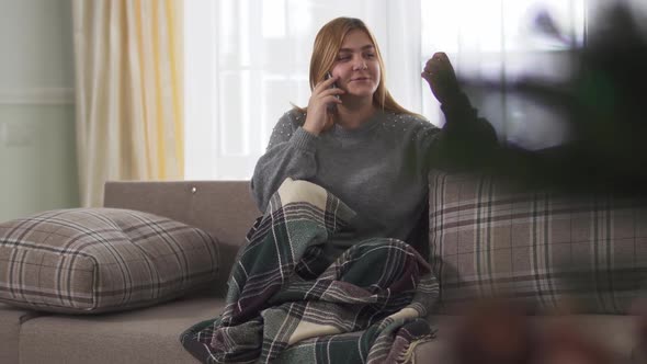 Chubby Woman Smiling While Speaking on Smart Phone Indoors Sitting Onder Blanket on the Sofa. Plus